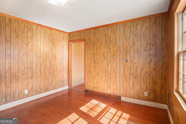 unfurnished room featuring a textured ceiling, baseboards, wood finished floors, and wooden walls