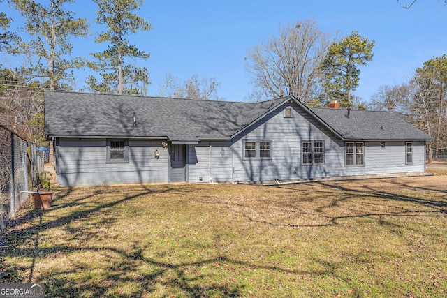 back of house featuring a shingled roof, a lawn, and fence