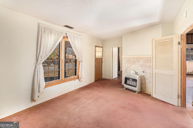 unfurnished living room with a textured ceiling, carpet flooring, visible vents, ornamental molding, and heating unit