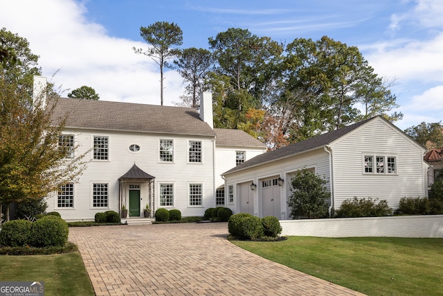 colonial inspired home with a garage, decorative driveway, a front yard, and a chimney