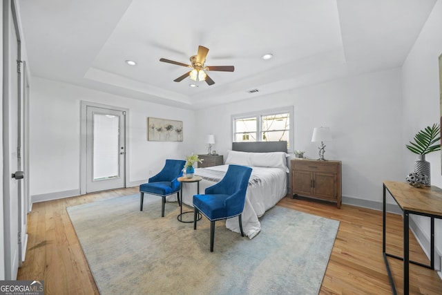 bedroom featuring light hardwood / wood-style floors, a tray ceiling, and ceiling fan