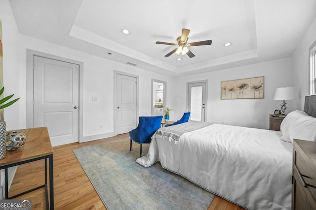 bedroom featuring ceiling fan, light hardwood / wood-style floors, a raised ceiling, and multiple windows