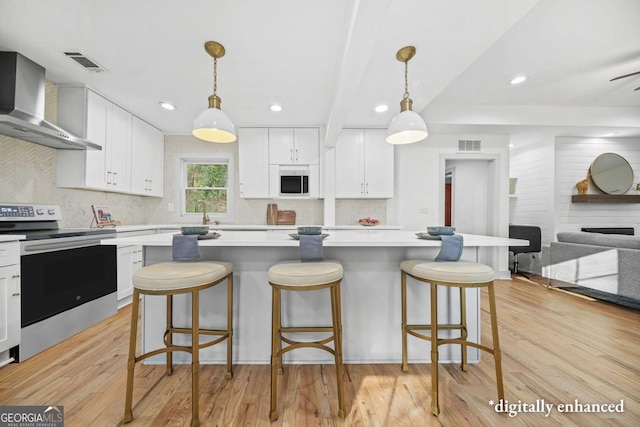 kitchen featuring electric stove, wall chimney range hood, white cabinetry, and hanging light fixtures