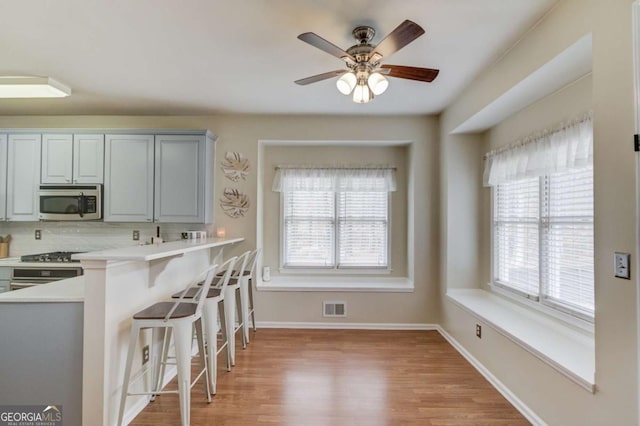 kitchen with visible vents, a kitchen breakfast bar, stainless steel appliances, light wood-style floors, and light countertops