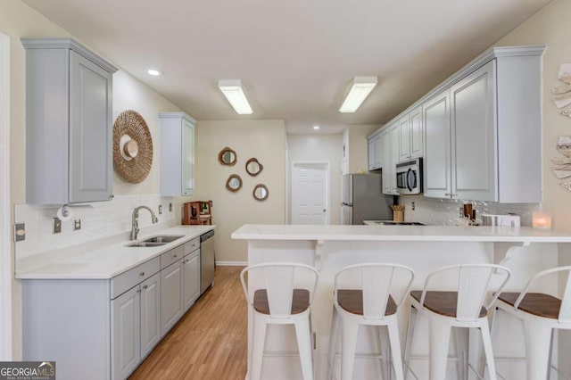 kitchen featuring gray cabinets, a sink, stainless steel appliances, a peninsula, and a breakfast bar area