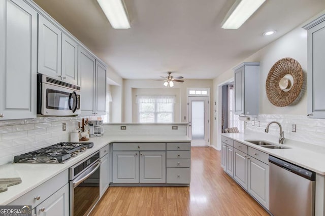 kitchen featuring gray cabinetry, a sink, stainless steel appliances, a peninsula, and light wood finished floors