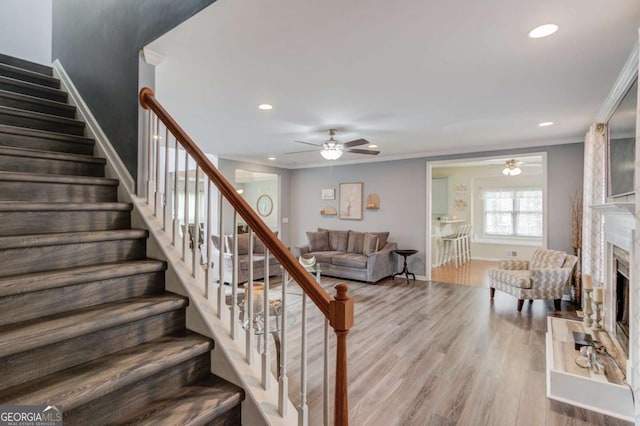 stairway featuring recessed lighting, a fireplace with raised hearth, wood finished floors, and ornamental molding