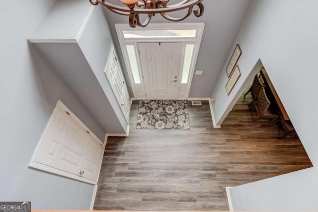 foyer entrance with visible vents, baseboards, an inviting chandelier, and wood finished floors