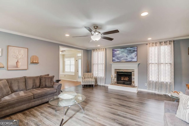 living area featuring a stone fireplace, a ceiling fan, baseboards, and wood finished floors