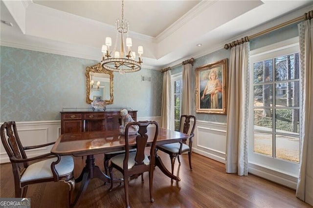 dining area with wood-type flooring, a notable chandelier, plenty of natural light, and a raised ceiling