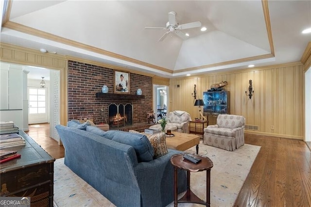 living room featuring ceiling fan, crown molding, hardwood / wood-style floors, a tray ceiling, and a brick fireplace