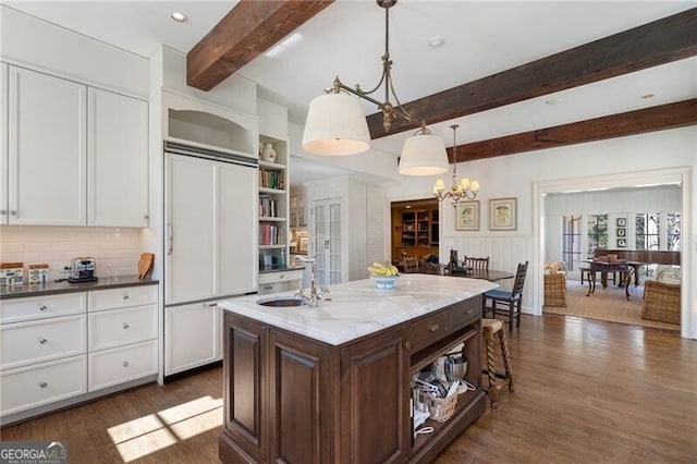 kitchen with white cabinetry, pendant lighting, dark stone counters, paneled built in fridge, and a kitchen island with sink