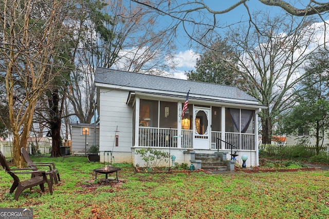 view of front facade featuring a shingled roof, an outdoor fire pit, a sunroom, and a front yard