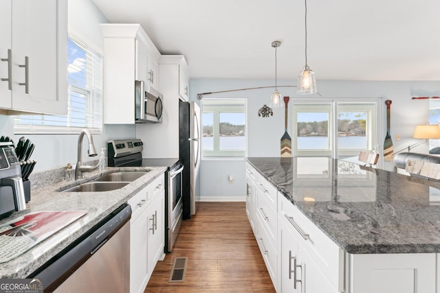 kitchen featuring dark stone counters, appliances with stainless steel finishes, white cabinetry, pendant lighting, and a sink