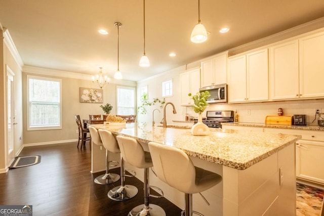 kitchen featuring appliances with stainless steel finishes, pendant lighting, crown molding, white cabinets, and an island with sink