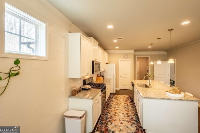 kitchen featuring a center island with sink, stainless steel appliances, decorative light fixtures, sink, and white cabinets