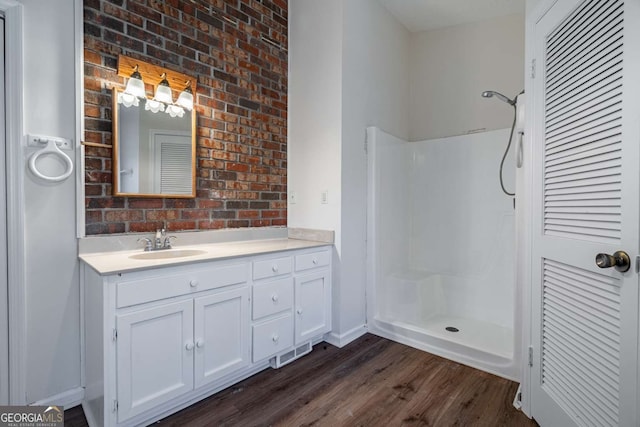 bathroom with a shower, hardwood / wood-style flooring, brick wall, and vanity