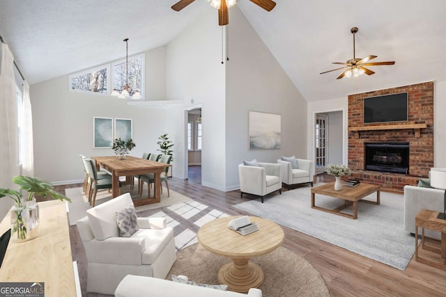 living room with ceiling fan with notable chandelier, light wood-type flooring, high vaulted ceiling, and a fireplace