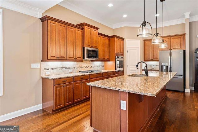 kitchen with a center island with sink, brown cabinets, decorative light fixtures, stainless steel appliances, and a sink