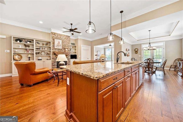 kitchen with open floor plan, a kitchen island with sink, crown molding, and decorative light fixtures