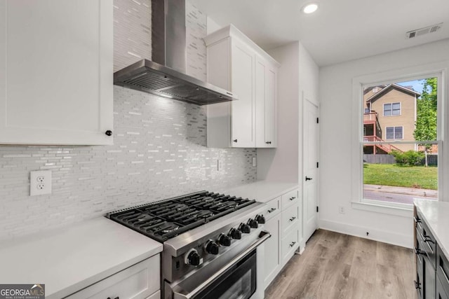 kitchen featuring light wood-type flooring, white cabinetry, wall chimney range hood, stainless steel gas range oven, and tasteful backsplash