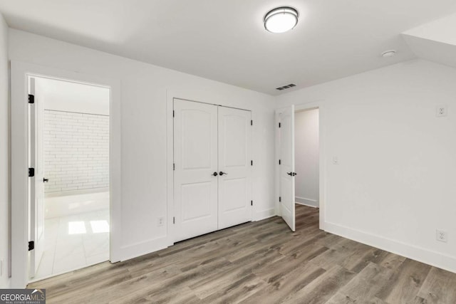 unfurnished bedroom with hardwood / wood-style flooring, ensuite bath, and a closet