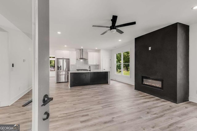 kitchen with a center island with sink, wall chimney range hood, light hardwood / wood-style floors, stainless steel fridge, and white cabinetry