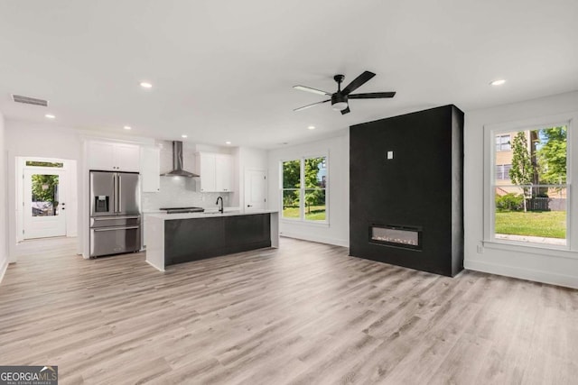 kitchen with a center island with sink, a wealth of natural light, white cabinetry, high quality fridge, and wall chimney exhaust hood