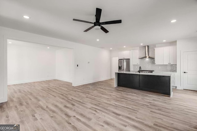 kitchen featuring a center island with sink, backsplash, stainless steel refrigerator with ice dispenser, wall chimney range hood, and white cabinets