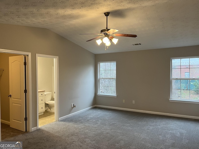 unfurnished bedroom with carpet floors, vaulted ceiling, a textured ceiling, and ensuite bath