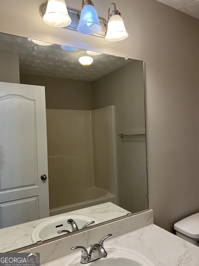 bathroom featuring toilet, vanity, a textured ceiling, and walk in shower