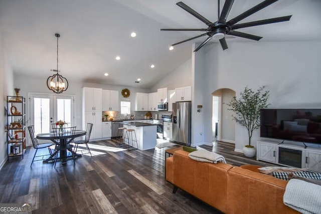 living room with dark wood-type flooring, high vaulted ceiling, and ceiling fan with notable chandelier