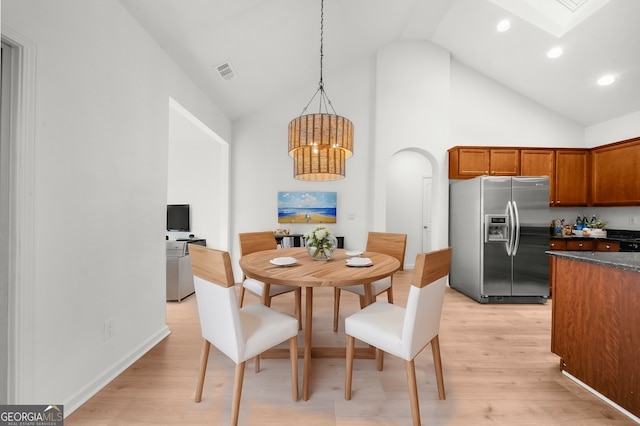 dining space with a skylight, high vaulted ceiling, an inviting chandelier, and light hardwood / wood-style floors