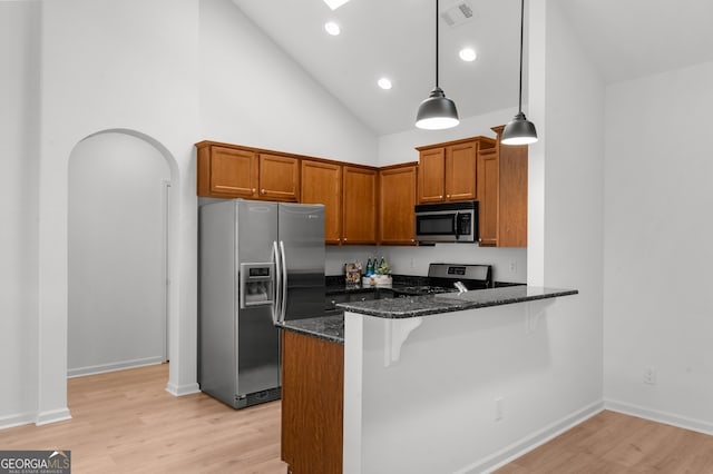 kitchen featuring dark stone countertops, appliances with stainless steel finishes, light wood-type flooring, decorative light fixtures, and kitchen peninsula