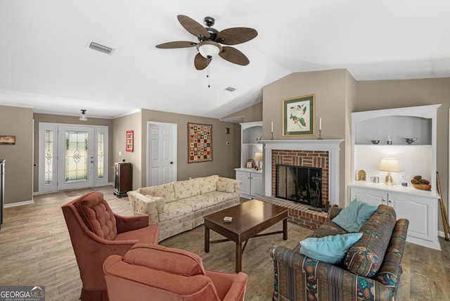 living room featuring built in shelves, lofted ceiling, ceiling fan, light hardwood / wood-style floors, and a brick fireplace