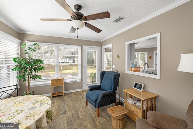 living area featuring a textured ceiling, ornamental molding, hardwood / wood-style flooring, and a healthy amount of sunlight