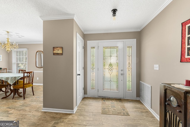 foyer featuring light wood-type flooring, a chandelier, crown molding, and a textured ceiling