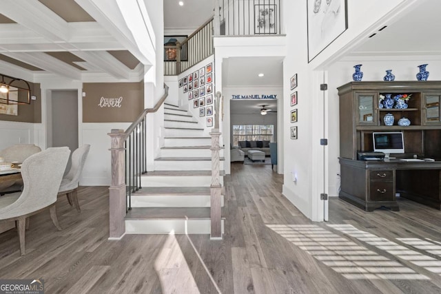 foyer with beam ceiling, a high ceiling, ceiling fan, wood-type flooring, and coffered ceiling