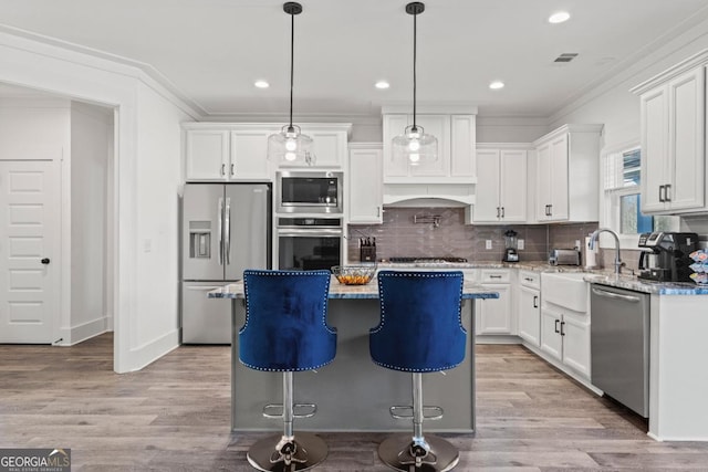 kitchen featuring sink, a kitchen island, stainless steel appliances, white cabinets, and hanging light fixtures