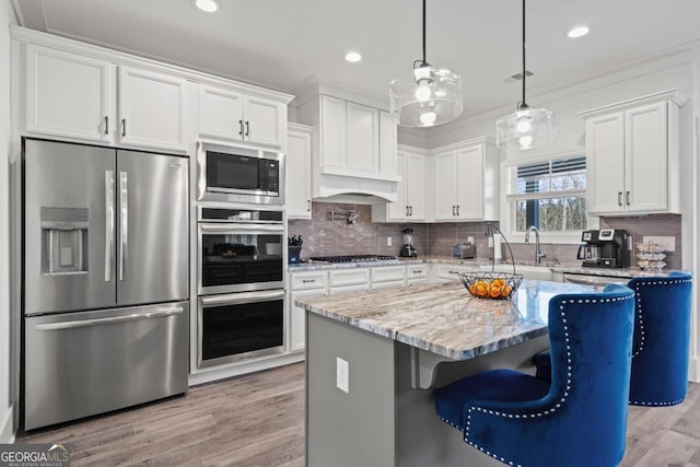 kitchen with appliances with stainless steel finishes, light stone counters, white cabinets, pendant lighting, and a center island