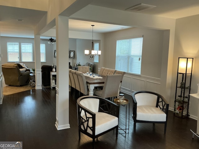 dining area featuring a healthy amount of sunlight, ceiling fan with notable chandelier, dark wood finished floors, and a decorative wall