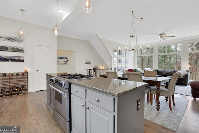 kitchen featuring stainless steel gas stove, pendant lighting, light stone countertops, and a kitchen island