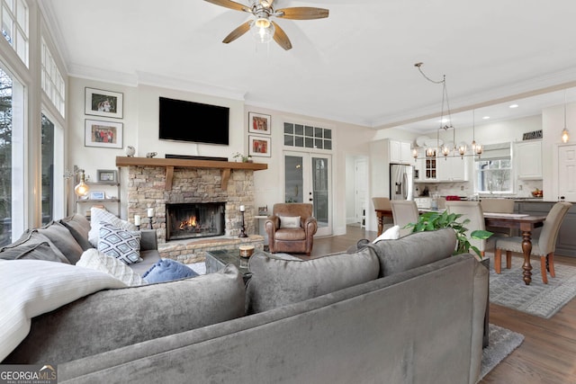 living room with ornamental molding, hardwood / wood-style floors, a stone fireplace, and ceiling fan with notable chandelier