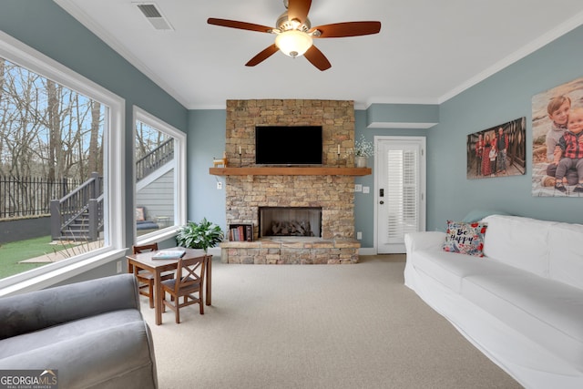 carpeted living room with ceiling fan, a stone fireplace, and ornamental molding