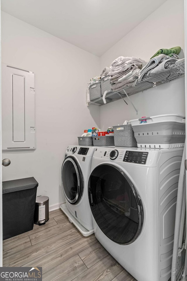 clothes washing area featuring light hardwood / wood-style flooring, washer and clothes dryer, and electric panel