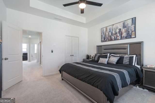 carpeted bedroom featuring a closet, ceiling fan, and a raised ceiling