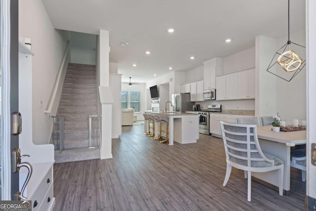 kitchen featuring a center island with sink, a kitchen bar, white cabinetry, pendant lighting, and stainless steel appliances