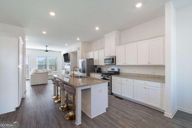 kitchen featuring sink, light stone counters, white cabinetry, stainless steel appliances, and a kitchen island with sink