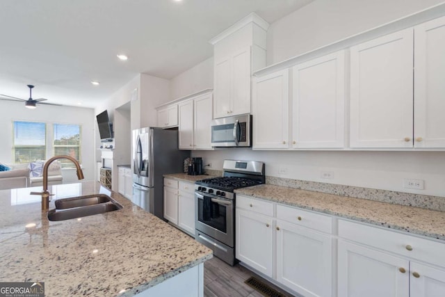 kitchen with white cabinetry, stainless steel appliances, light stone countertops, and sink