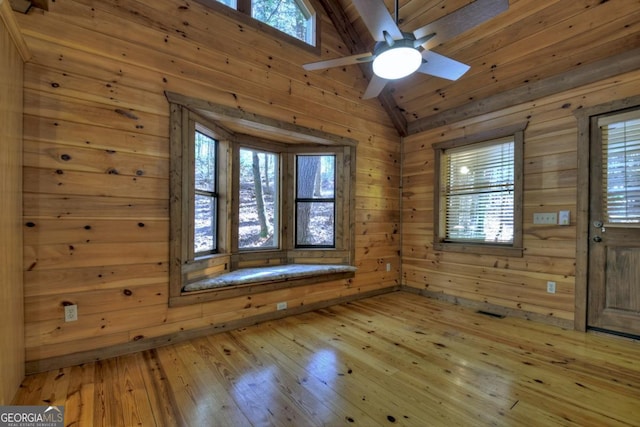 interior space with light wood-type flooring, lofted ceiling, plenty of natural light, and wood walls